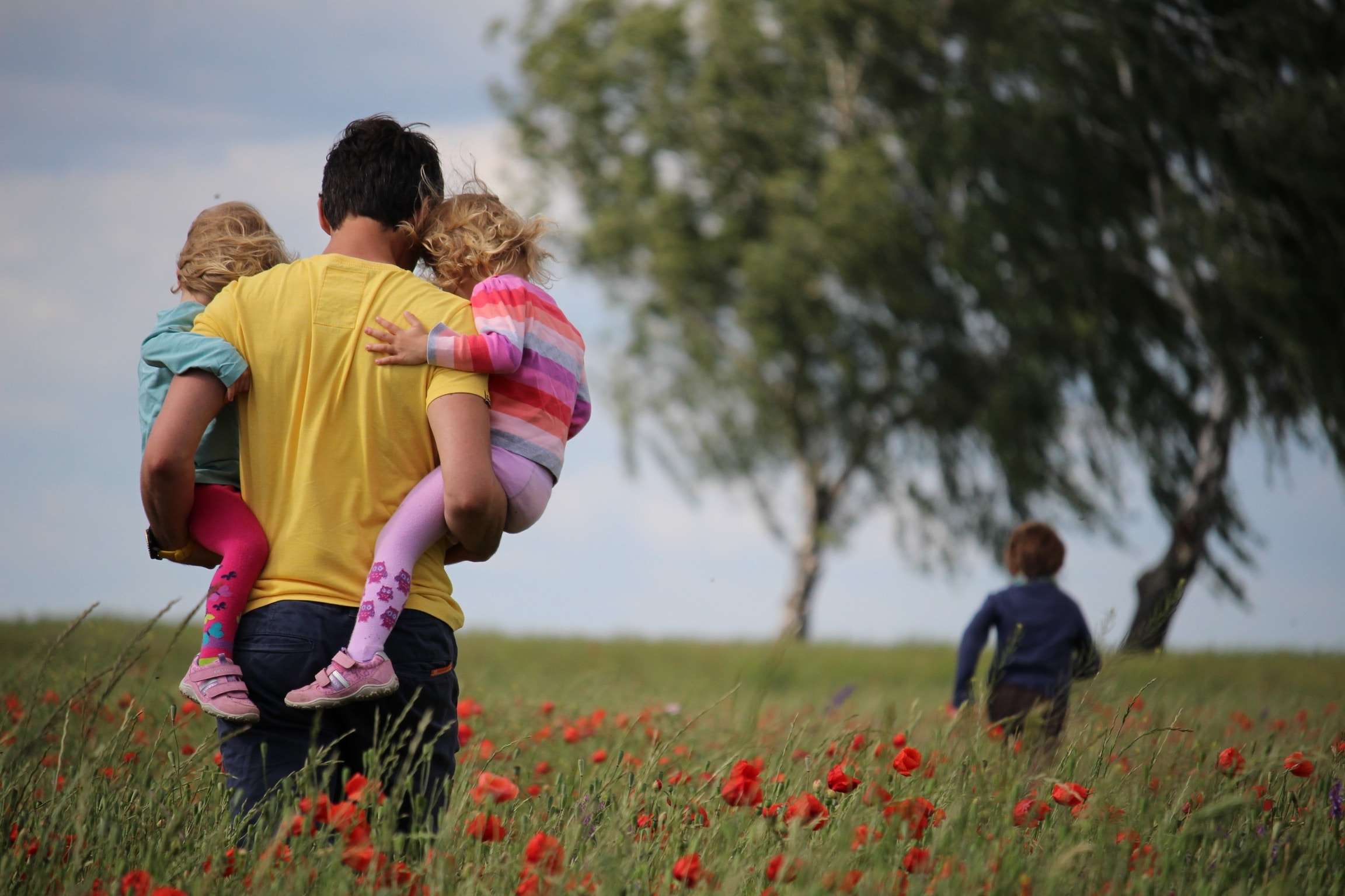 man holding twins walking through a field