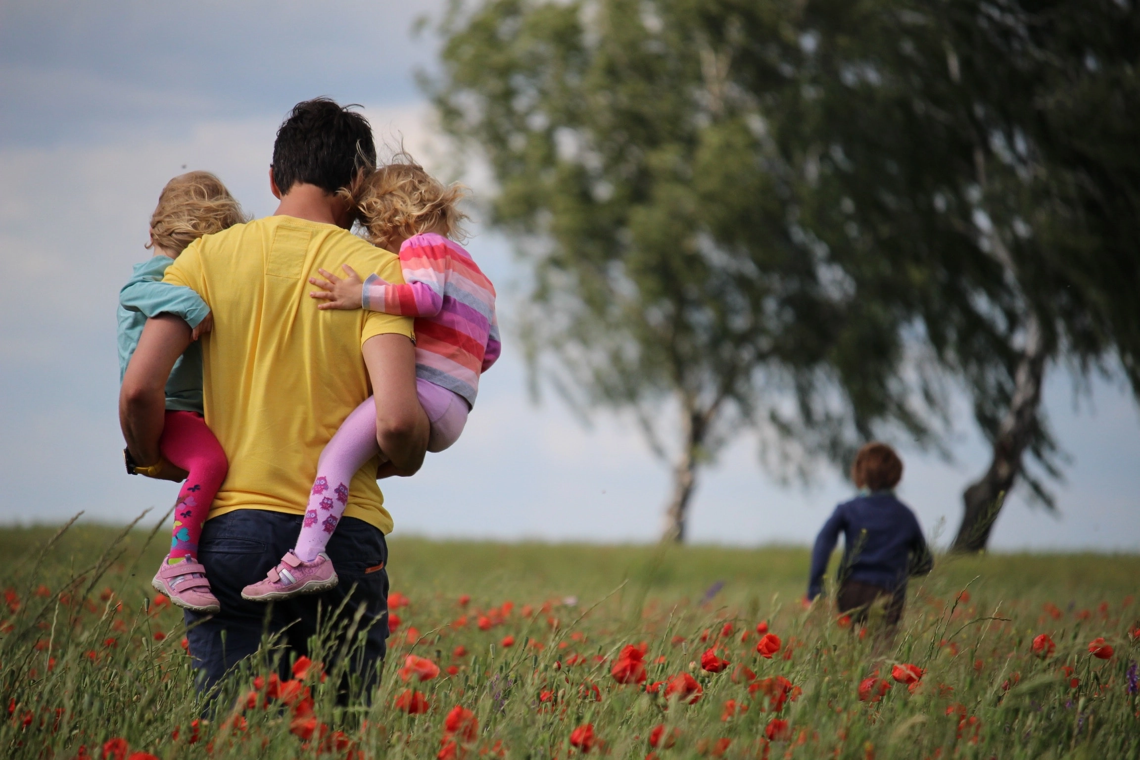 man holding twins walking through a field